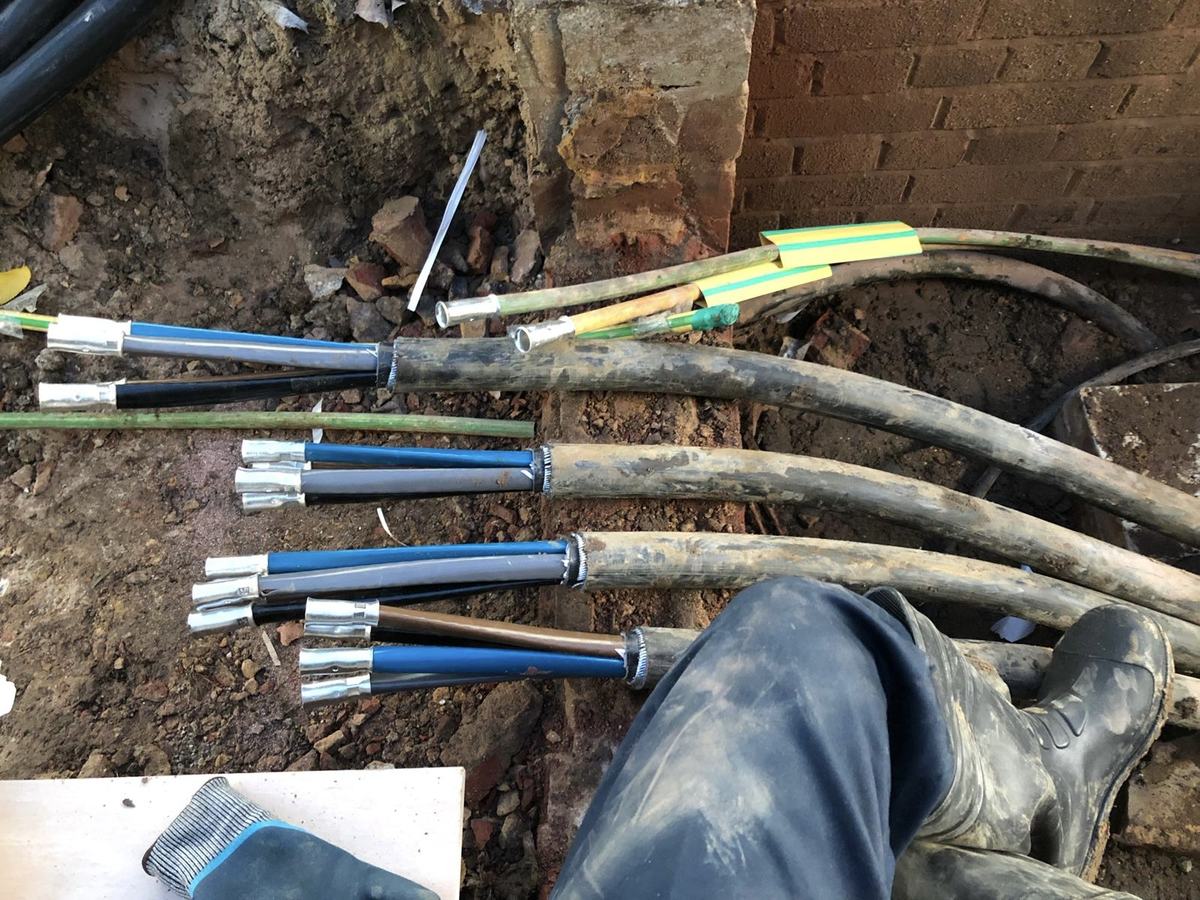 Armoured cable tails glanded and terminated in an excavated trench against a brick wall — photograph 18 of 25