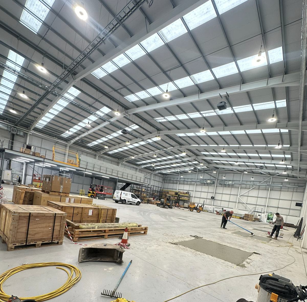 First fix under way across the floor of a new industrial unit, high-bay lighting already live overhead — photograph 21 of 25