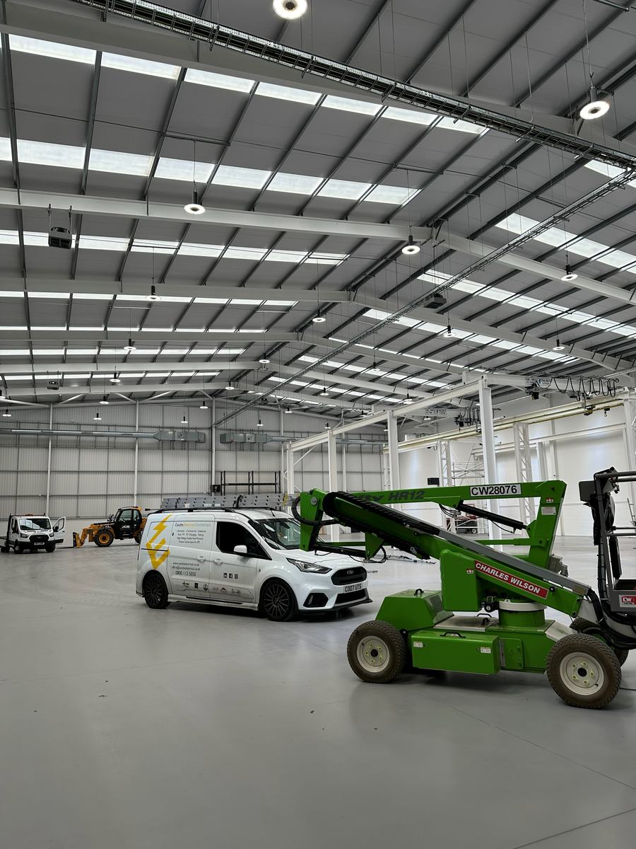 A Coutts Electrical Contractors van and a boom lift inside a workshop during a high-level installation — photograph 22 of 25